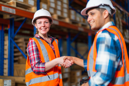 Two warehouse workers shaking hand when success project or first time greeting in a distribution...