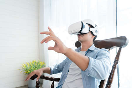 Asian man wearing virtual reality goggles in living room at home. VR technology and innovation concept.の写真素材
