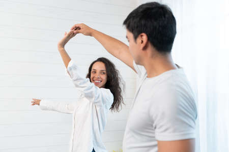 Happy young couple dancing together in the living room at home. Cheerful man and woman dancing together at homeの写真素材