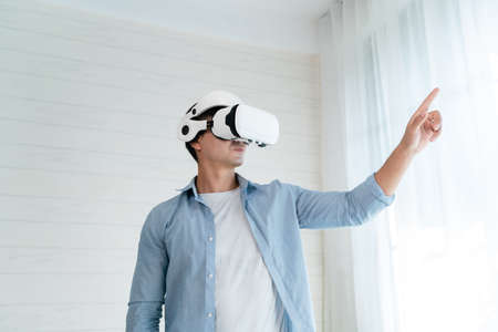 Asian man wearing virtual reality goggles in the living room at home.の写真素材