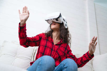 Young woman wearing virtual reality goggles sitting on sofa at home. Technology and entertainment concept.の写真素材