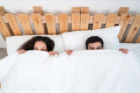 Couple lying in bed at home, looking at camera and smilingの写真素材