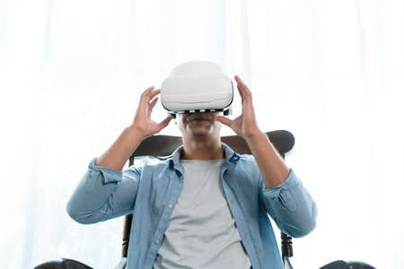 Mature man wearing virtual reality headset while sitting in chair at homeの写真素材