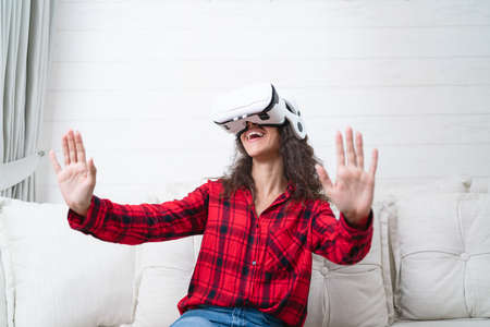Young woman wearing virtual reality goggles sitting on the sofa at home.の写真素材