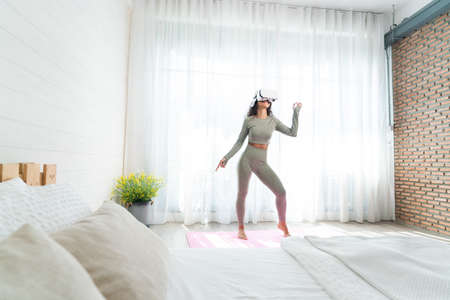 Young woman wearing virtual reality glasses while practicing yoga on the bed at homeの写真素材