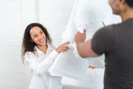 Young woman in white shirt and black man in white shirt are having fun with pillows.の写真素材