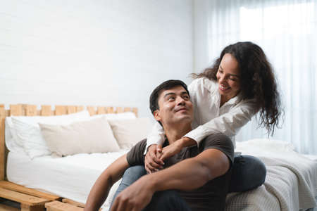 Portrait of young asian man and woman sitting on bed in bedroom.の写真素材