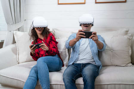 Young couple playing video games with virtual reality headset on sofa at homeの写真素材