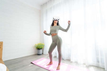 Young asian woman wearing virtual reality glasses practicing yoga at home.の写真素材