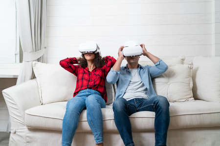 Young couple wearing virtual reality goggles while sitting on sofa at home.の写真素材