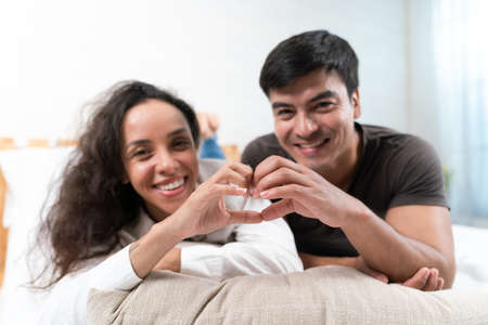 Happy asian couple holding a heart shape on the bed at homeの写真素材