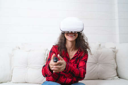 Woman playing video games with virtual reality headset on sofa at home.の写真素材