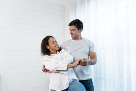 Happy young couple dancing in the living room at home. Cheerful man and woman dancing togetherの写真素材