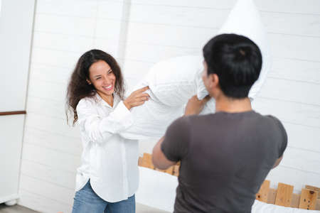 Young couple fighting with pillows in bedroom, focus on the womanの写真素材
