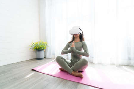 Young woman wearing virtual reality headset while doing yoga exercise at home.の写真素材