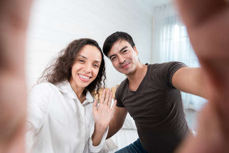 Happy young couple taking selfie with mobile phone in living room at homeの写真素材