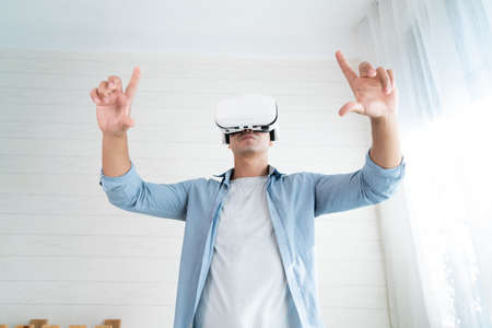 Young man wearing virtual reality goggles at home. Technology and entertainment concept.の写真素材