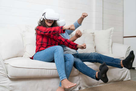 Happy young woman using virtual reality headset while sitting on sofa at homeの写真素材