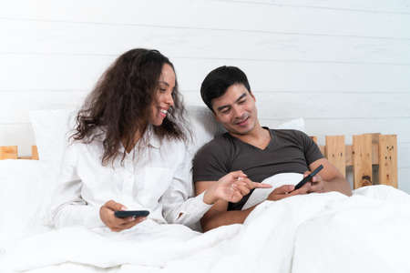 Happy couple using mobile phone while lying on bed at home. Lifestyle conceptの写真素材