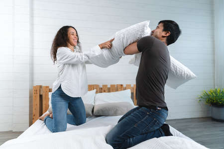 Happy Asian couple having pillow fight in bedroom at home. Lifestyle and love concept.の写真素材