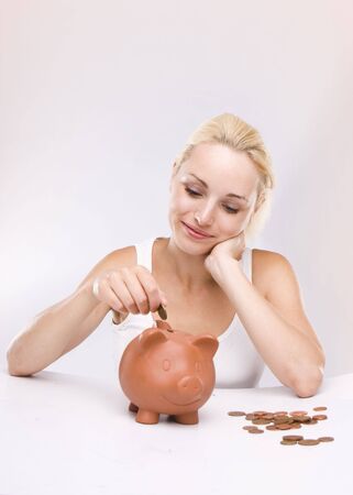 Young lady looking at pink piggy bank isolated over white backgroundの写真素材