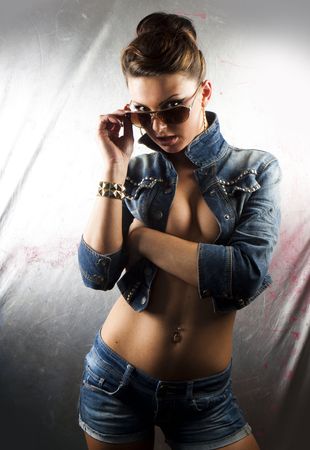 Sexy brunette woman wearing short denim jacket, jeans with belly button ring, bracelet, and hoop earrings against a graffiti covered wall.の写真素材