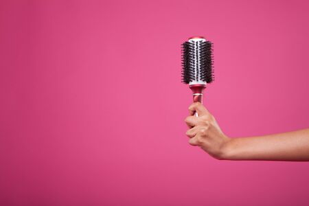 woman hand holding hairbrush on pink backgroundの写真素材