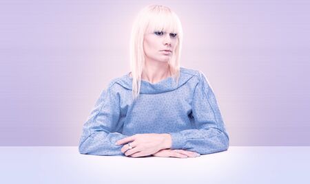 Attractive young blond woman seated at table with studio background.の写真素材