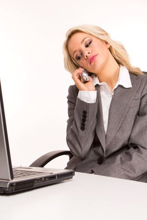 Portrait of an sexy business woman sitting by a desk and laptop speaking over the phone , smiling の写真素材