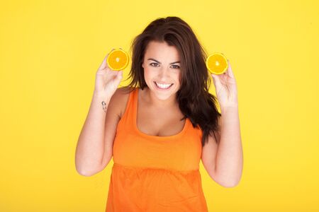 Cute Cheeky Woman Having Fun With Oranges, beautiful woman with cheeky smile holding up two orange slicesの写真素材