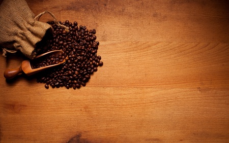 Freshly roasted coffee beans spilling out of a hessian bag over a wooden scoop and onto a textured wooden background with copyspaceの写真素材