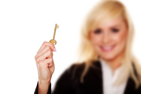 A blonde woman holds up a golden brass key in her hand isolated on white with selective focus to the keyの写真素材