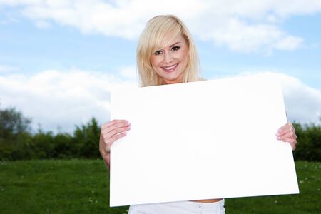 Blonde woman holding empty sign outside with sky backgroundの写真素材