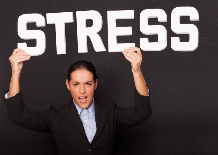 Stressed angry attractive businesswoman holding up the word STRESS in white lettering high above her head on a black studio backgroundの写真素材