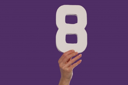 Female hand holding up the number 8 against a purple background conceptual of numbers, measurement, amount, quantity, accounting and mathematicsの写真素材