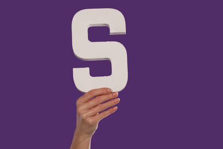 Female hand holding up the uppercase capital letter S isolated against a purple background...