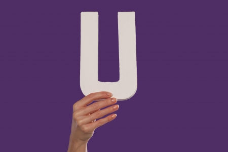 Female hand holding up the uppercase capital letter U isolated against a purple background conceptual of the alphabet, writing, literature and typefaceの写真素材