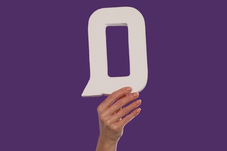 Female hand holding up the uppercase capital letter Q isolated against a purple background conceptual of the alphabet, writing, literature and typefaceの写真素材