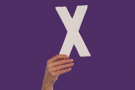 Female hand holding up the uppercase capital letter x isolated against a purple background conceptual of the alphabet, writing, literature and typefaceの写真素材