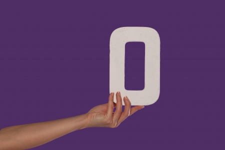 Female hand holding up the number 0 against a purple background conceptual of numbers, measurement, amount, quantity, accounting and mathematicsの写真素材