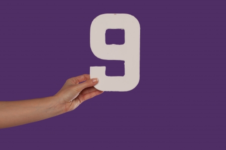 Female hand holding up the number 9 against a purple background conceptual of numbers, measurement, amount, quantity, accounting and mathematicsの写真素材