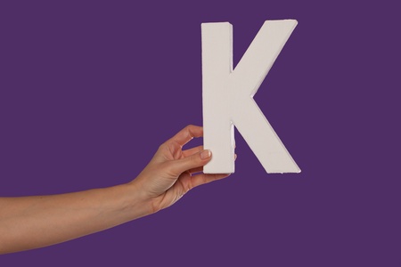 Female hand holding up the uppercase capital letter K isolated against a purple background conceptual of the alphabet, writing, literature and typefaceの写真素材