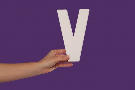 Female hand holding up the uppercase capital letter V isolated against a purple background conceptual of the alphabet, writing, literature and typefaceの写真素材