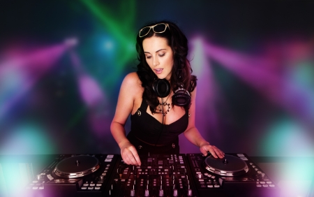 Glamorous sexy busty DJ at work mixing sound on her decks at a party or night club with colourful strobe light backgroundの写真素材