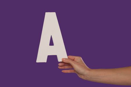 Female hand holding up the uppercase capital letter A isolated against a purple background conceptual of the alphabet, writing, literature and typefaceの写真素材