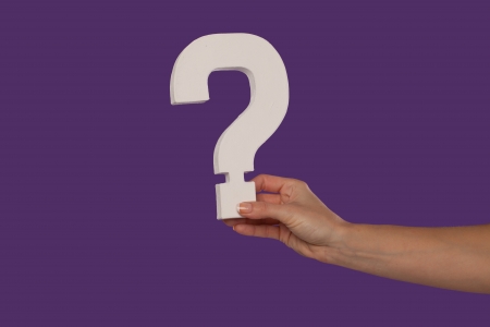 Female hand holding up a white question mark against a purple background conceptual of questions, query, why or what.の写真素材