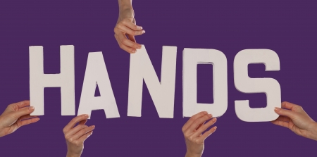 White alphabet lettering spelling HANDS held up over a purple studio background by outstreched female handsの写真素材
