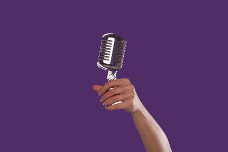 Female hand holding up a microphone over a purple studio backgroundの写真素材