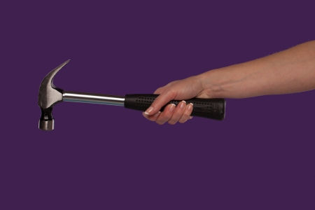 Female hand holding a steel claw hammer over a purple studio background in a DIY, home maintenance and construction conceptの写真素材