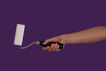 Hand of a female decorator holding a paint roller over a purple studio background in a DIY, renovation and home redecorating conceptの写真素材